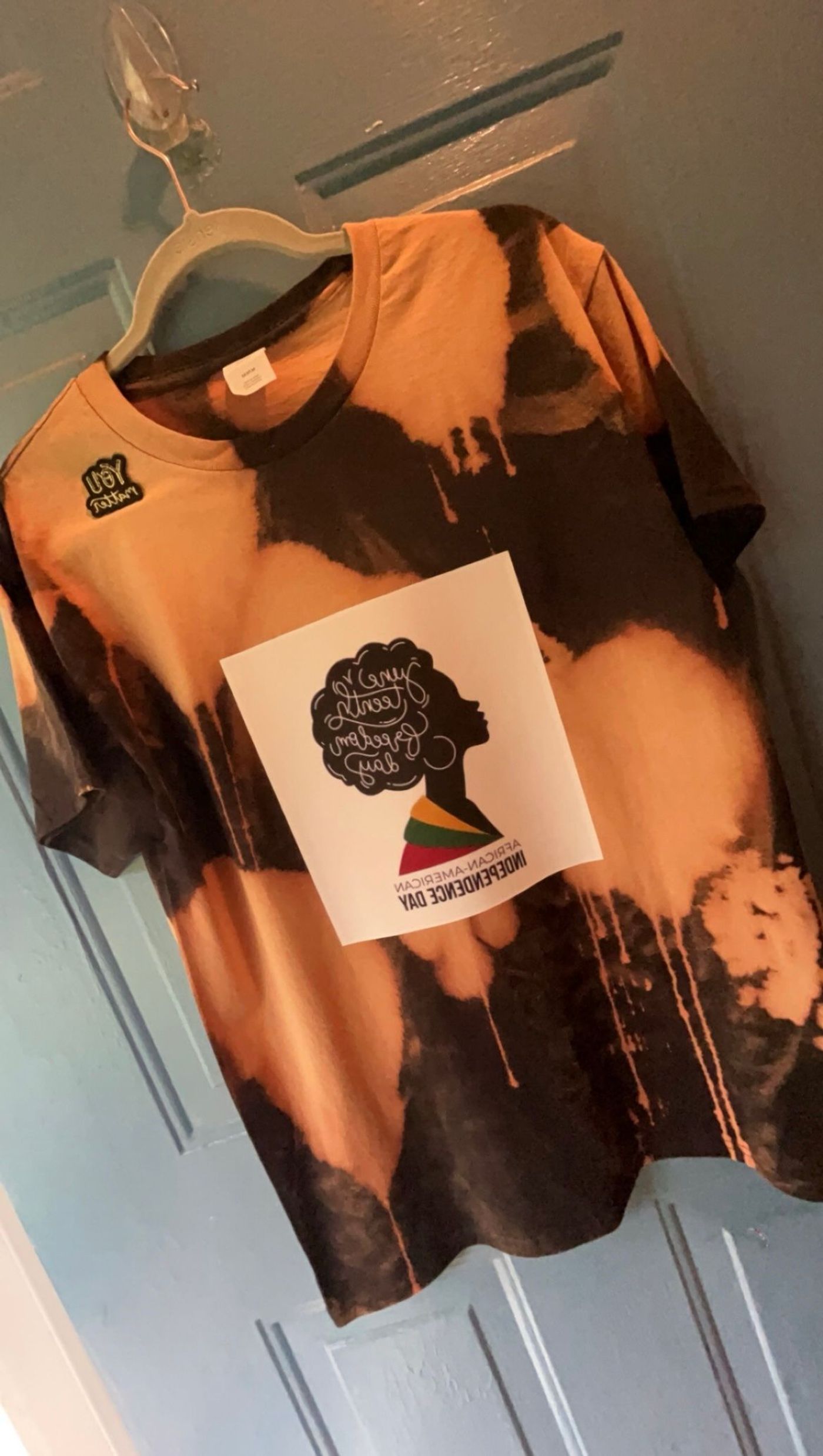 A reverse bleach-dyed tee in orange and black on a hanger
